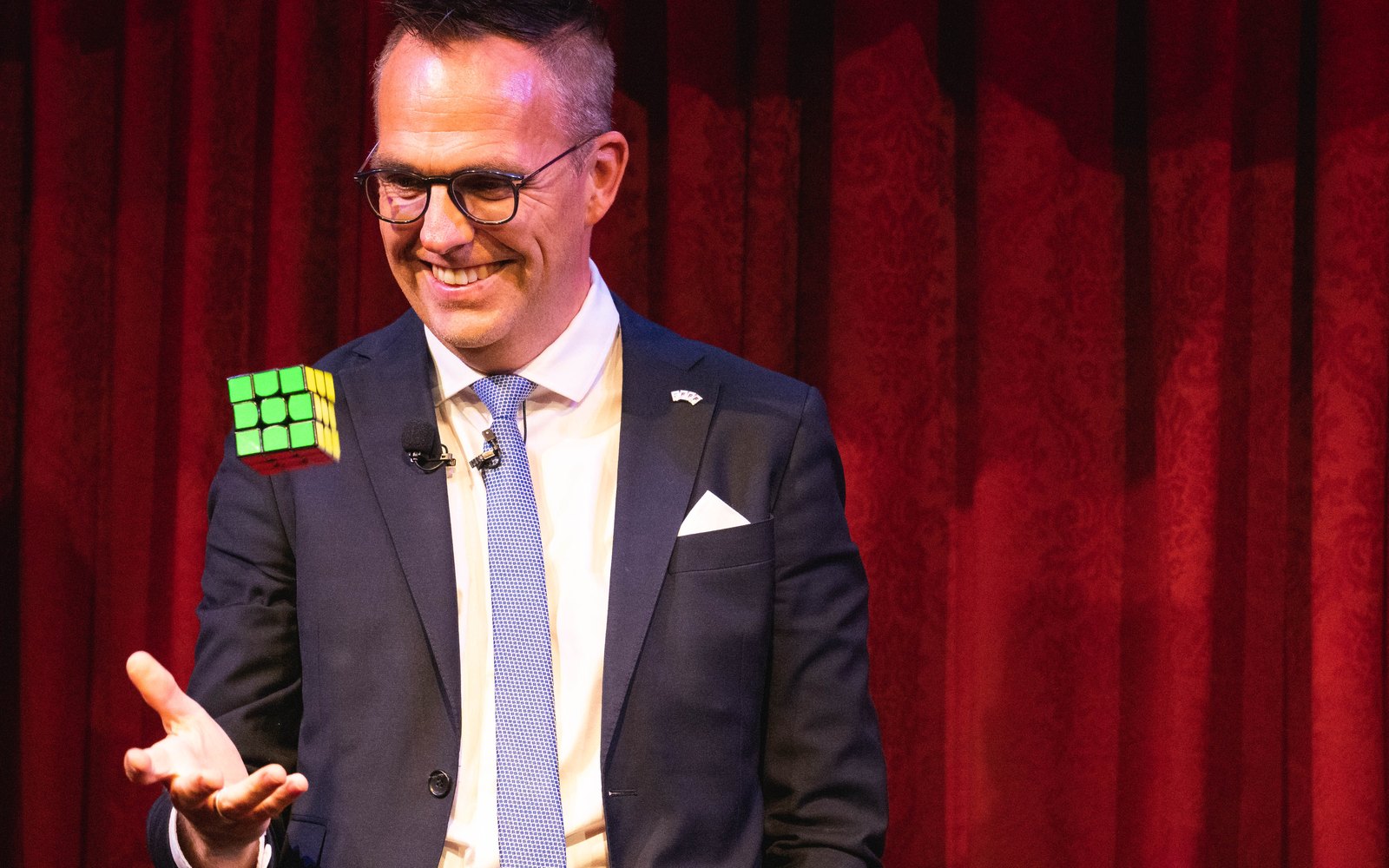 Rune Carlsen skaper et magisk øyeblikk med Rubiks kube foran rød scenegardin.
